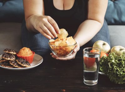 Woman choosing to eat junk food chips instead of swapping for healthy vegetables