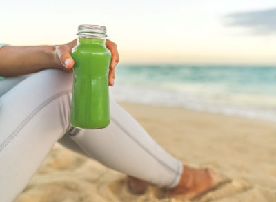 Woman holding green juice beach