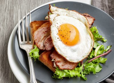 Fried egg on a blt sandwich on gray plate with fork