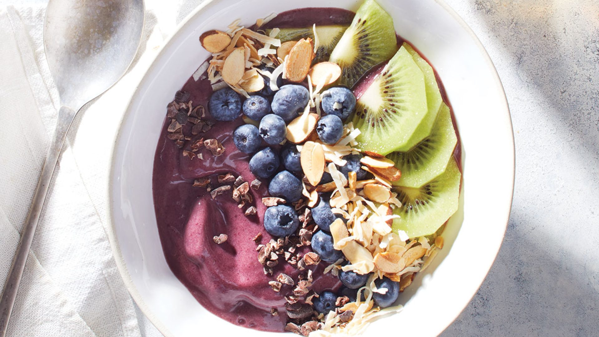 acai bowl with blueberries and kiwi in white bowl with spoon