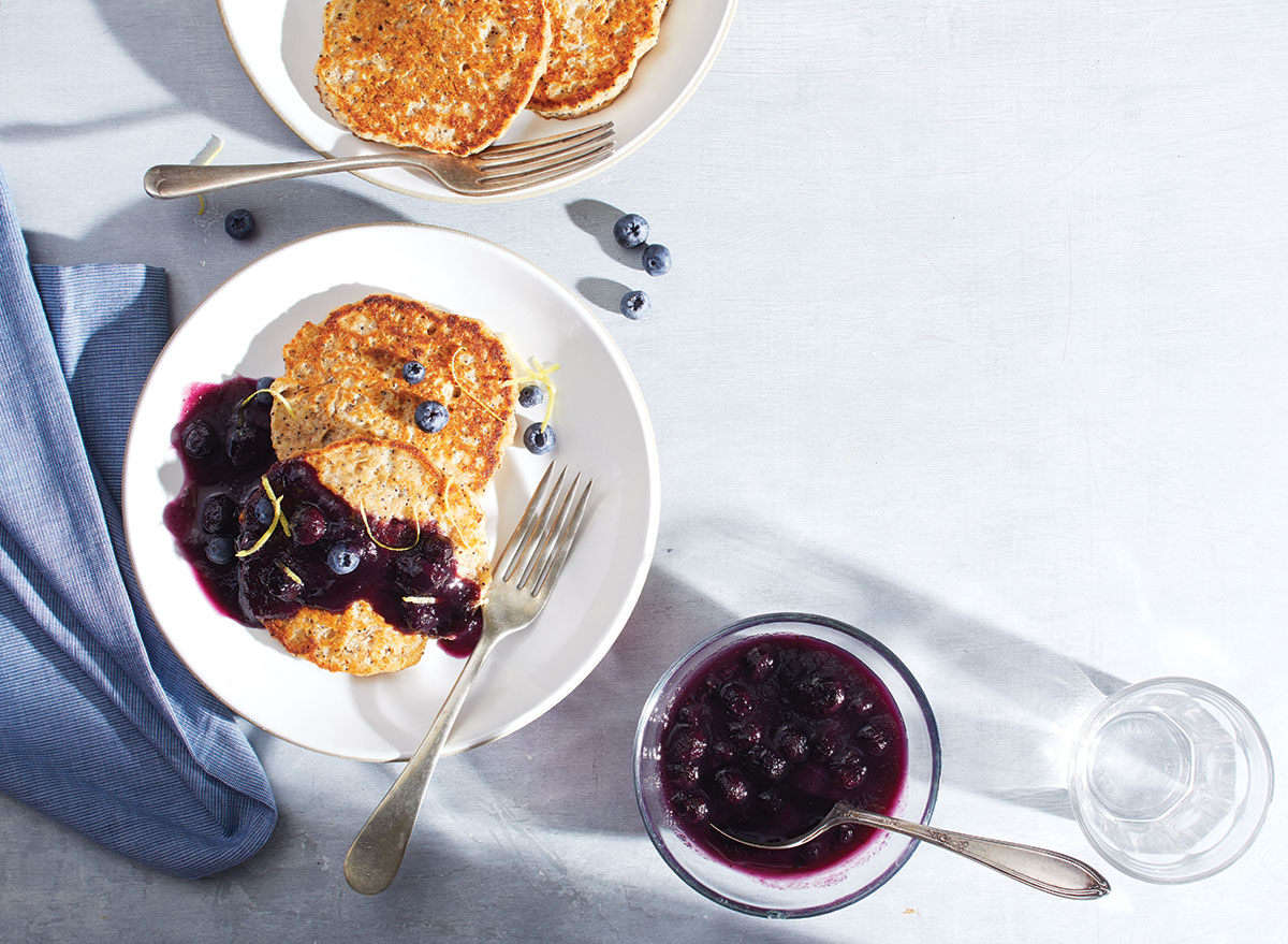 maanzaadpannenkoeken met bosbessencompote op wit bord met vork, lepel, blauw doek servet