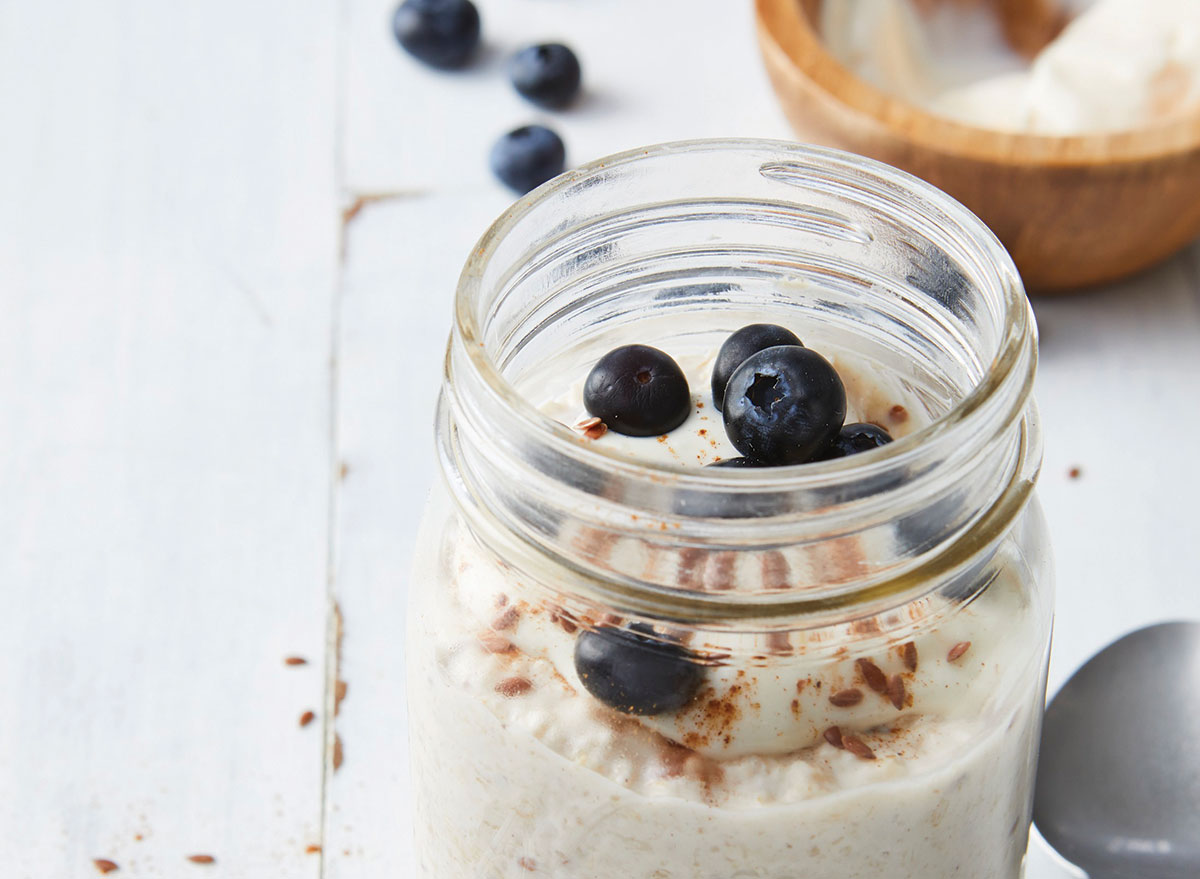 overnight cinnamon roll oats i åpent glass mason jar med blåbær på tre bordplaten med skje