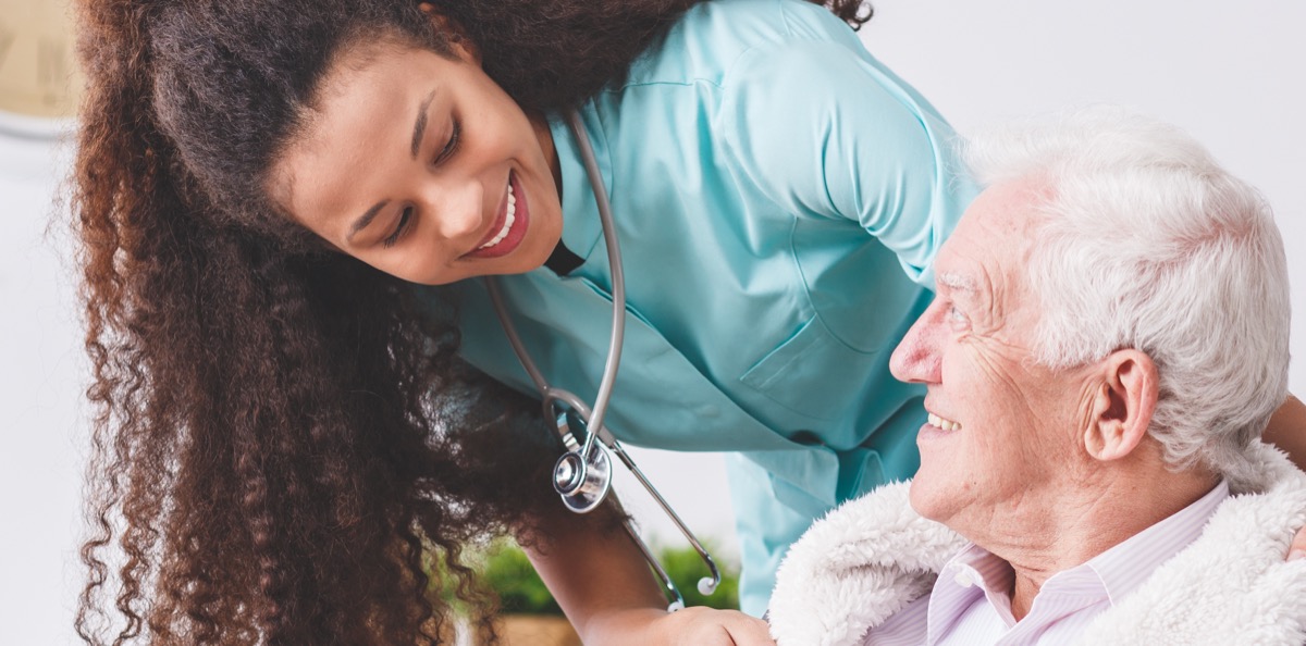 nurse with a stethoscope covering an elderly man with a blanket in a nursing home