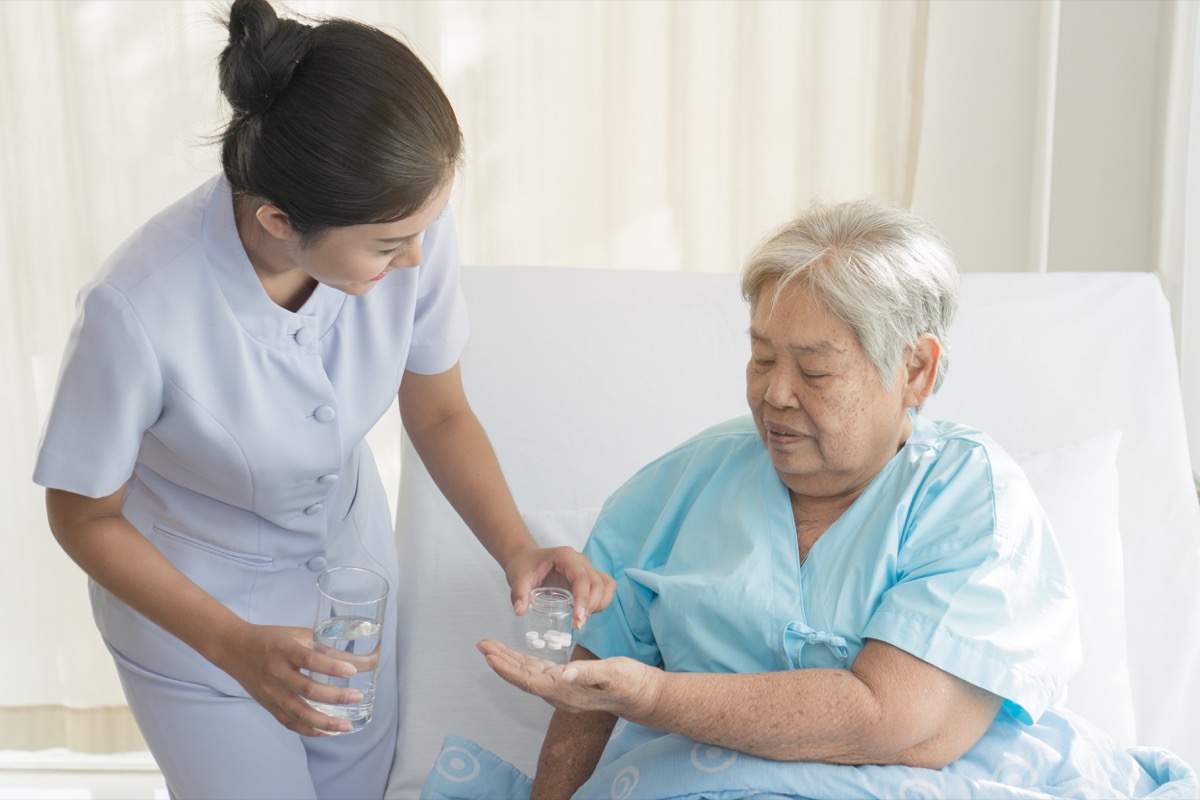 caregiver nurse helping elderly woman taking medicine on the bed and check up after admit inpatient in hospital