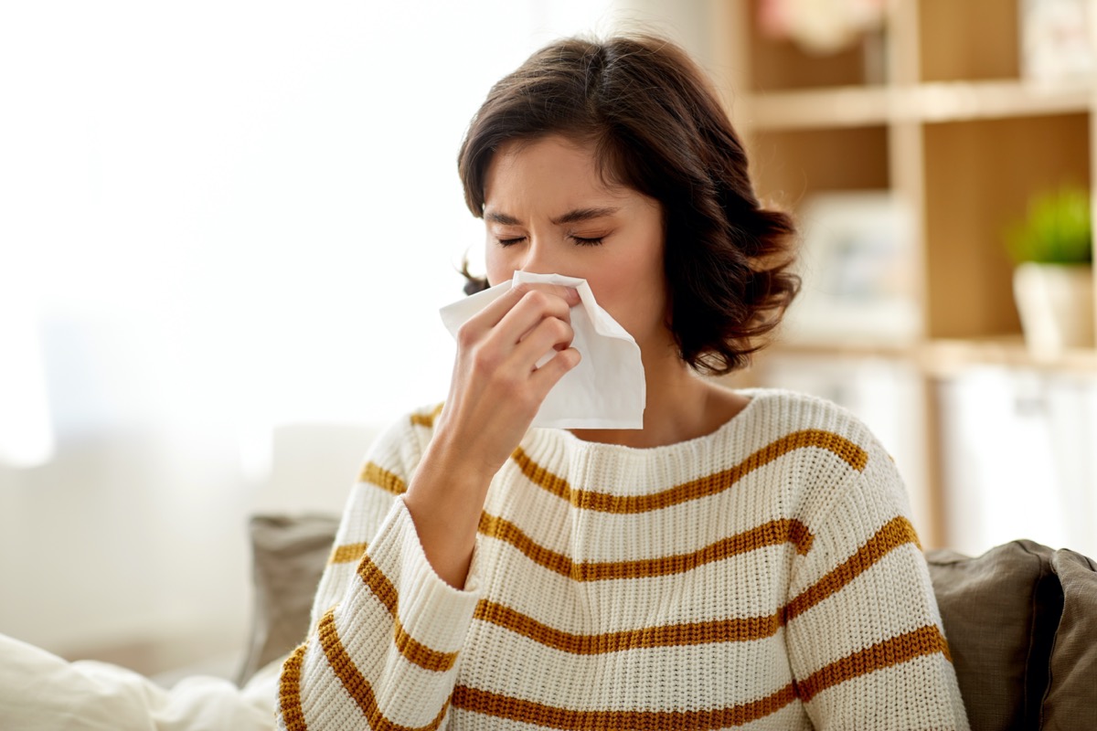 Sick woman blowing her runny nose in paper tissue at home.
