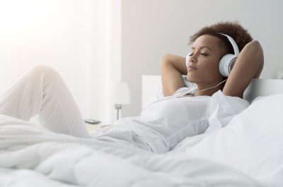 woman relaxing and listening to music using headphones, she is lying in bed