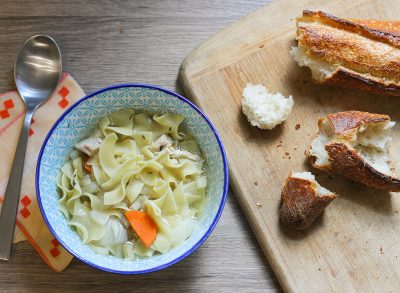 Crock pot chicken noodle soup with bread on a table.