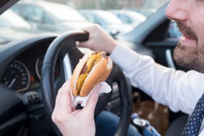 Man eating an hamburger while driving car