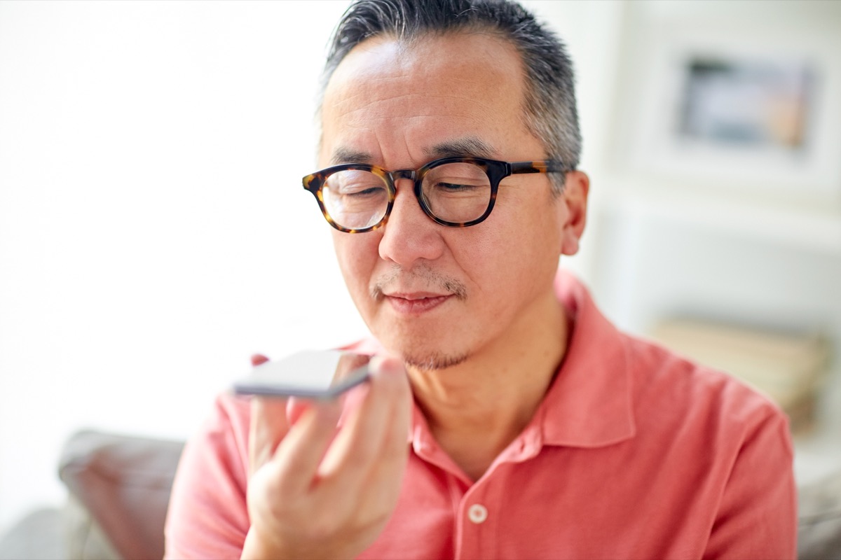 happy man using voice command recorder on smartphone at home