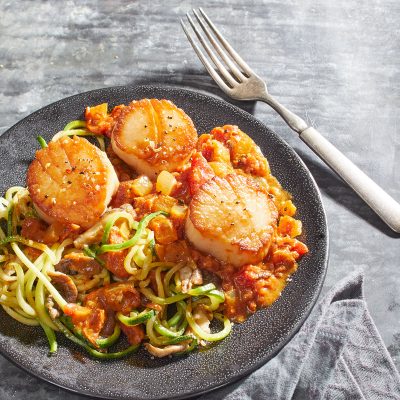 keto thai curry with scallops, zucchini noodles, and shiitake mushrooms on a gray plate with fork