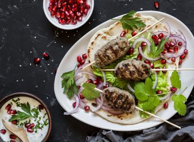 lamb kebabs on a plate with pomegranate seeds and fresh veggies