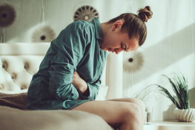 Young upset stressed woman suffering from abdominal and stomach pain during menstruation, PMS in room at home. Inflammation and infection. Food poisoning