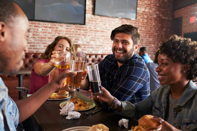 Friends Eating Out In Sports Bar With Screens In Background