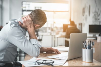 Man holding sore neck while using notebook