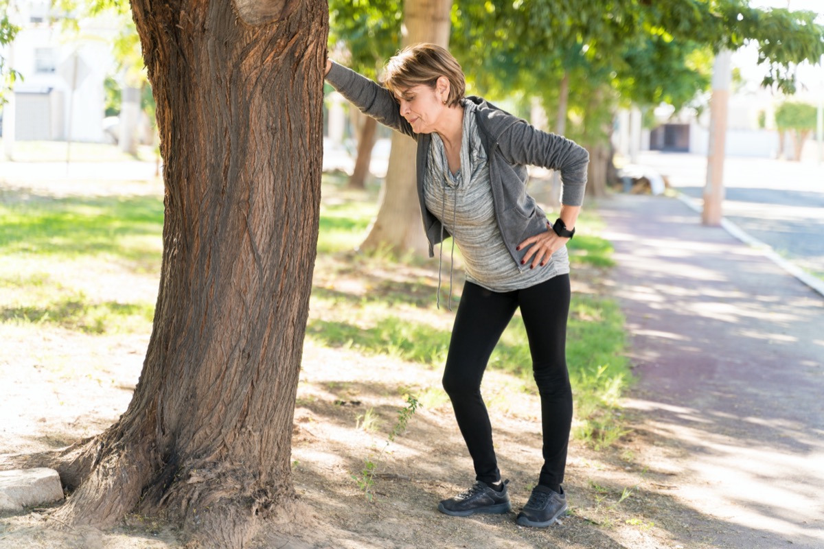 Full length of exhausted senior woman taking a break while leaning on tree in city
