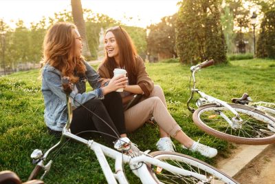 Image of two young beautiful women friends outdoors with bicycles in park.