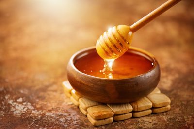 Honey dripping from honey dipper in wooden bowl