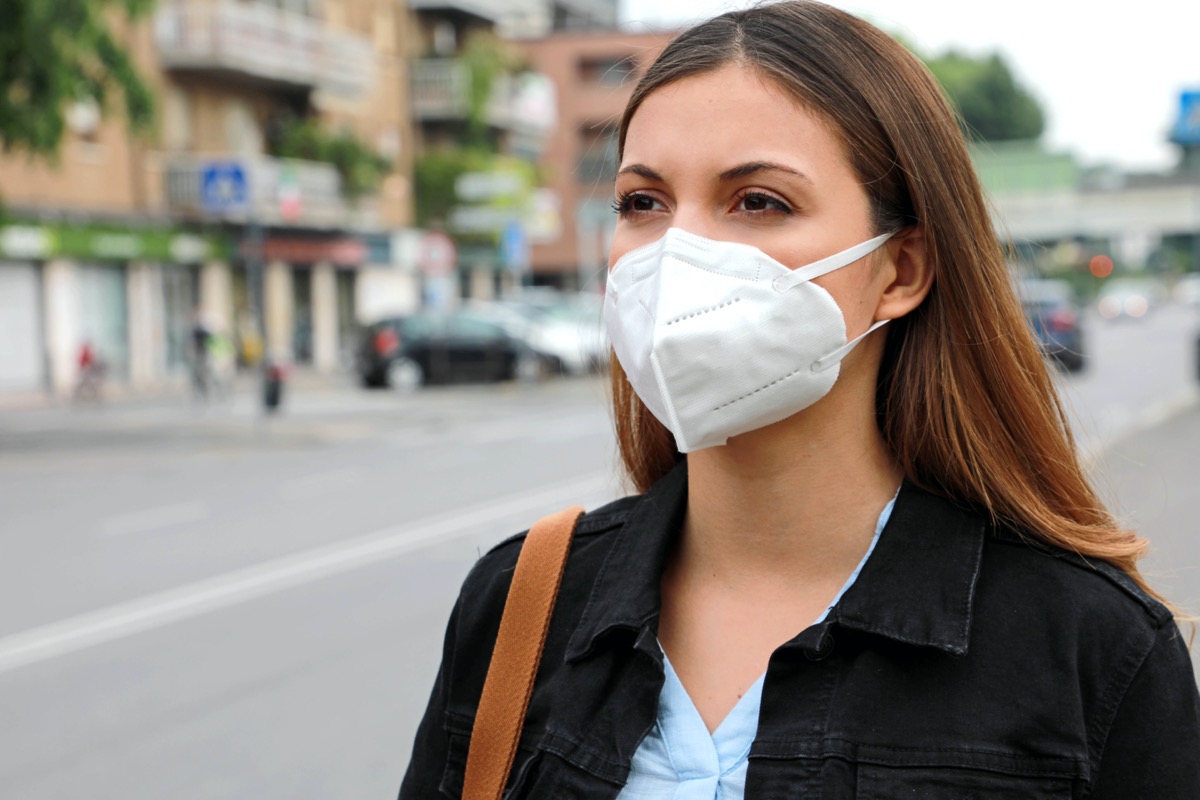 Woman in city street wearing KN95 FFP2 mask protective for spreading of disease virus SARS-CoV-2.