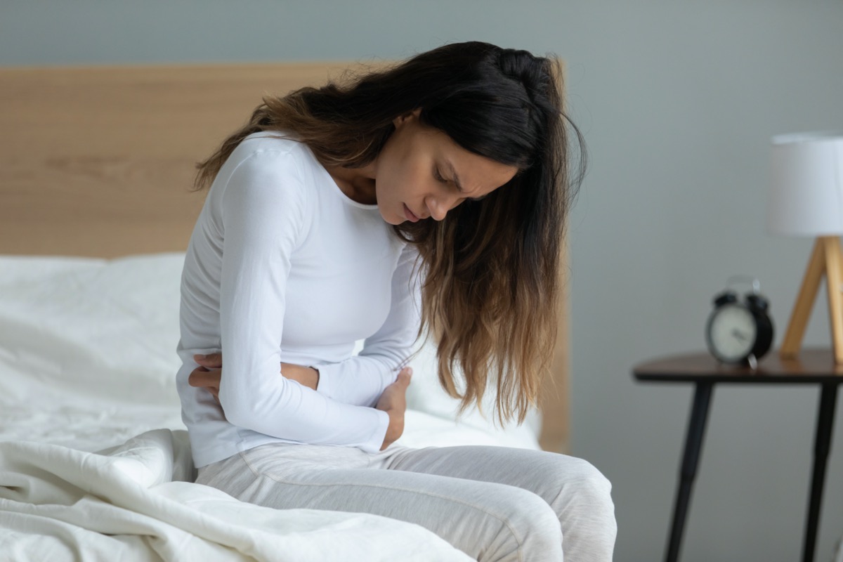 Unhealthy woman sit on bed touch stomach