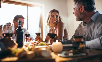 Smiling woman talking with friends sitting at dining tablet at home. Group of people having great time at dinner party.