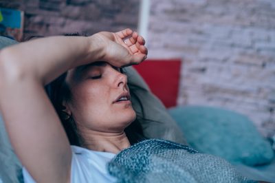 Sick young woman lying in the bed covered with blanket