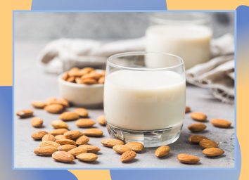 glass of almond milk with almonds laying around it