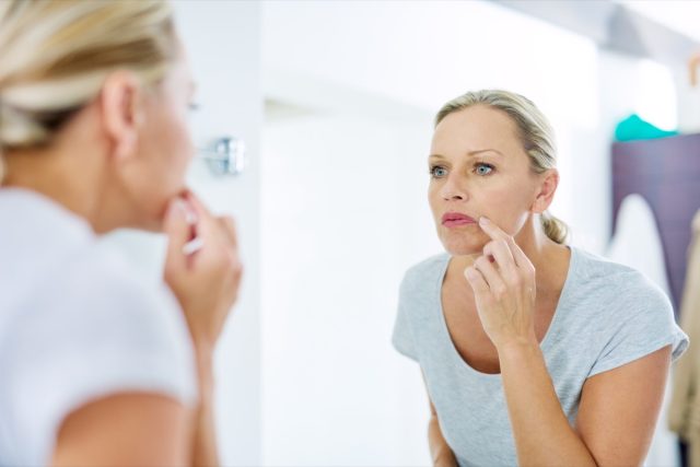 A mature woman inspects her skin in front of a mirror in the bathroom.