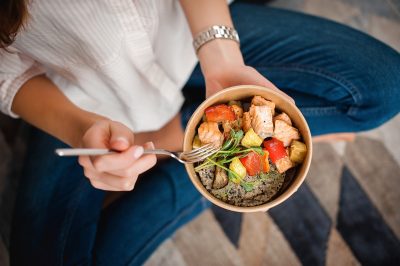 woman holding bowl of vegetables, fish, and rice