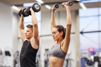 sport, fitness, lifestyle and people concept - smiling man and woman with dumbbells flexing muscles in gym