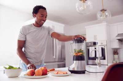 young man making smoothie in modern kitchen