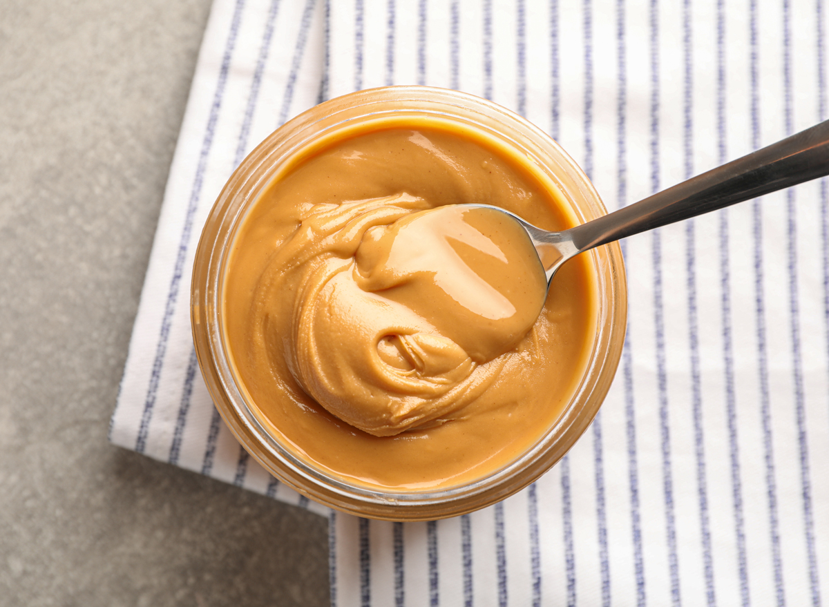 An opened jar of peanut butter with a small spoon Stock Photo