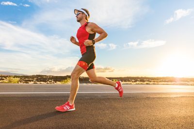 Triathlon - Triathlete man running in triathlon suit training for ironman race. Male runner exercising on Big Island Hawaii. Sunset.