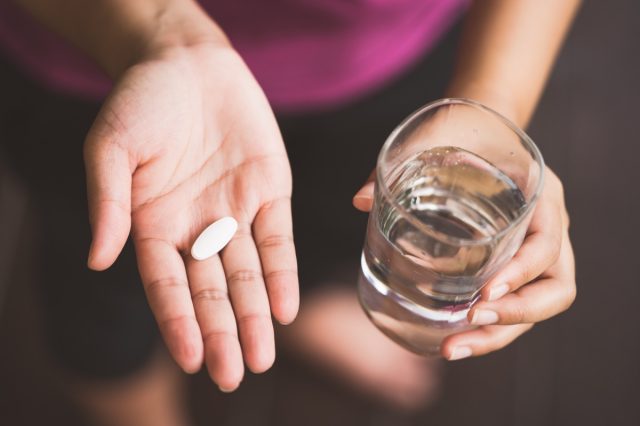 woman holding collagen supplement and glass of water