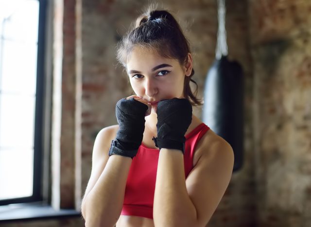 Young woman ready for hits punching bag during a boxing training. Female boxer doing fitness. Regular sports boosts immune system and promote good health and resistance to diseases. Healthy lifestyle