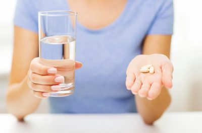 woman in blue crew neck t-shirt holding glass of water and handful of supplements