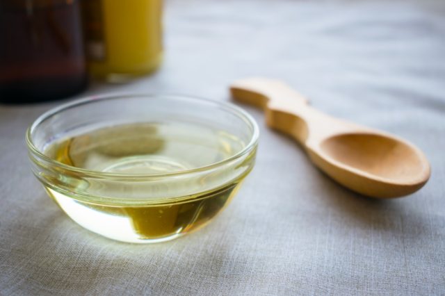 Liquid coconut MCT oil in round glass bowl with wooden spoon and bottles.