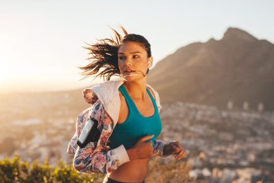 woman jogs at sunset on hill overlooking city