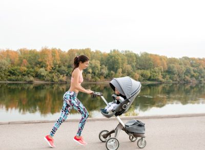 woman in athletic attire jogging with her baby in a stroller along lake