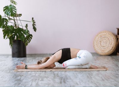 woman does child's pose on bamboo mat in pink room