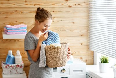 happy woman smelling clean laundry next to washing machine