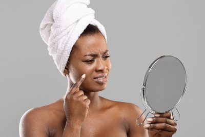 woman looks in mirror at pimple