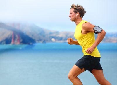 man in bright yellow tank sprints by water