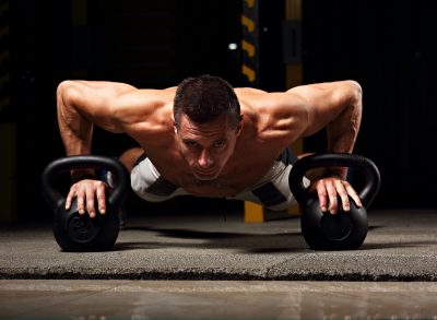 man doing pushups with kettlebells to build pecs