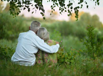 old senior couple snuggling outside looking out into lush park