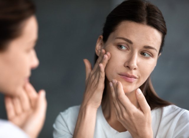 woman looking at acne spot on chin in mirror