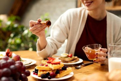 woman adding honey to a plate of healthy protein waffles