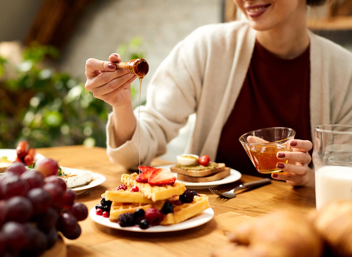 woman adding honey to a plate of healthy protein waffles