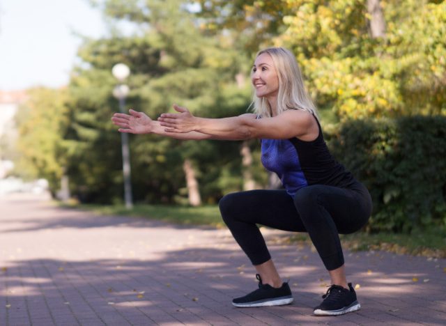 middle-aged woman doing bodyweight squat outside during walk