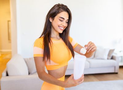 woman adding fitness supplements, protein powder to beverage