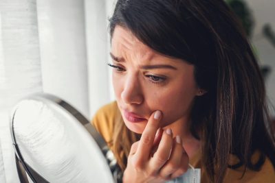 woman concerned look on face looking in mirror skin cancer